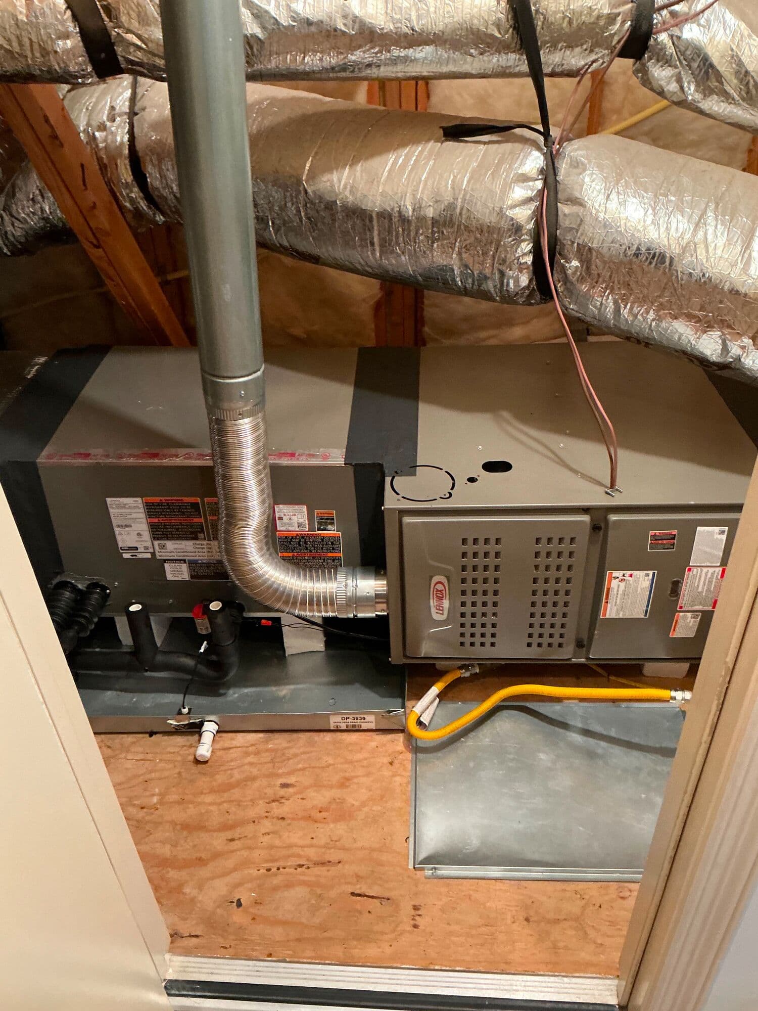 Attic mechanical platform: a Lennox gas furnace with its yellow flexible gas connector and sheet-metal plenum beside a second cabinet, its flue elbow rising past insulated flex ducts.