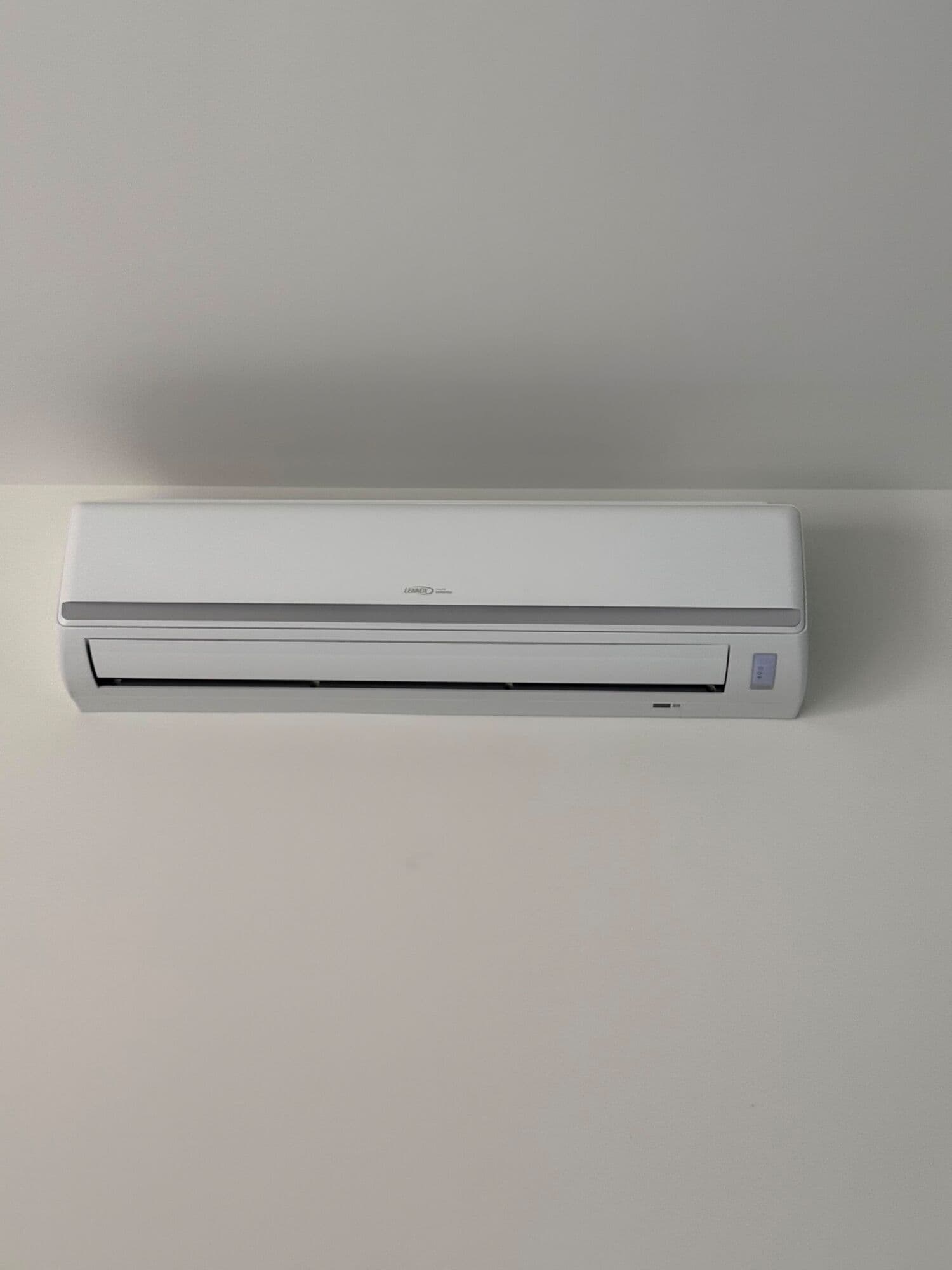 Lennox ductless mini-split head mounted high on a plain white interior wall, louver closed, with no exposed pipework on the finished face of the wall.
