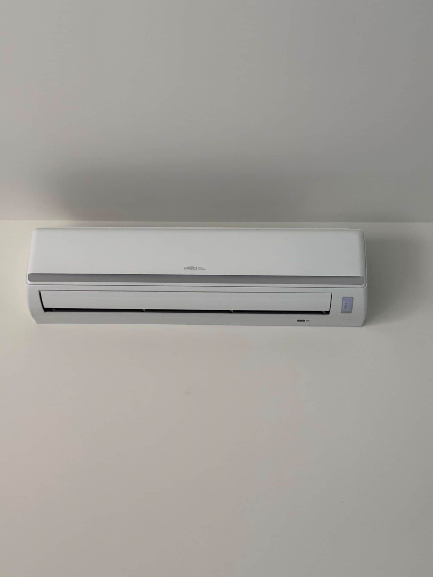 Lennox ductless mini-split head mounted high on a plain white interior wall, louver closed, with no exposed pipework on the finished face of the wall.